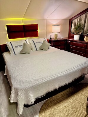 A hotel room with a large bed, a headboard with integrated lighting, a bedside table with a lamp, and a potted plant.