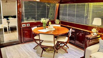 A spacious dining area with a round table and chairs, a small side table with a lamp, and a view through large windows.