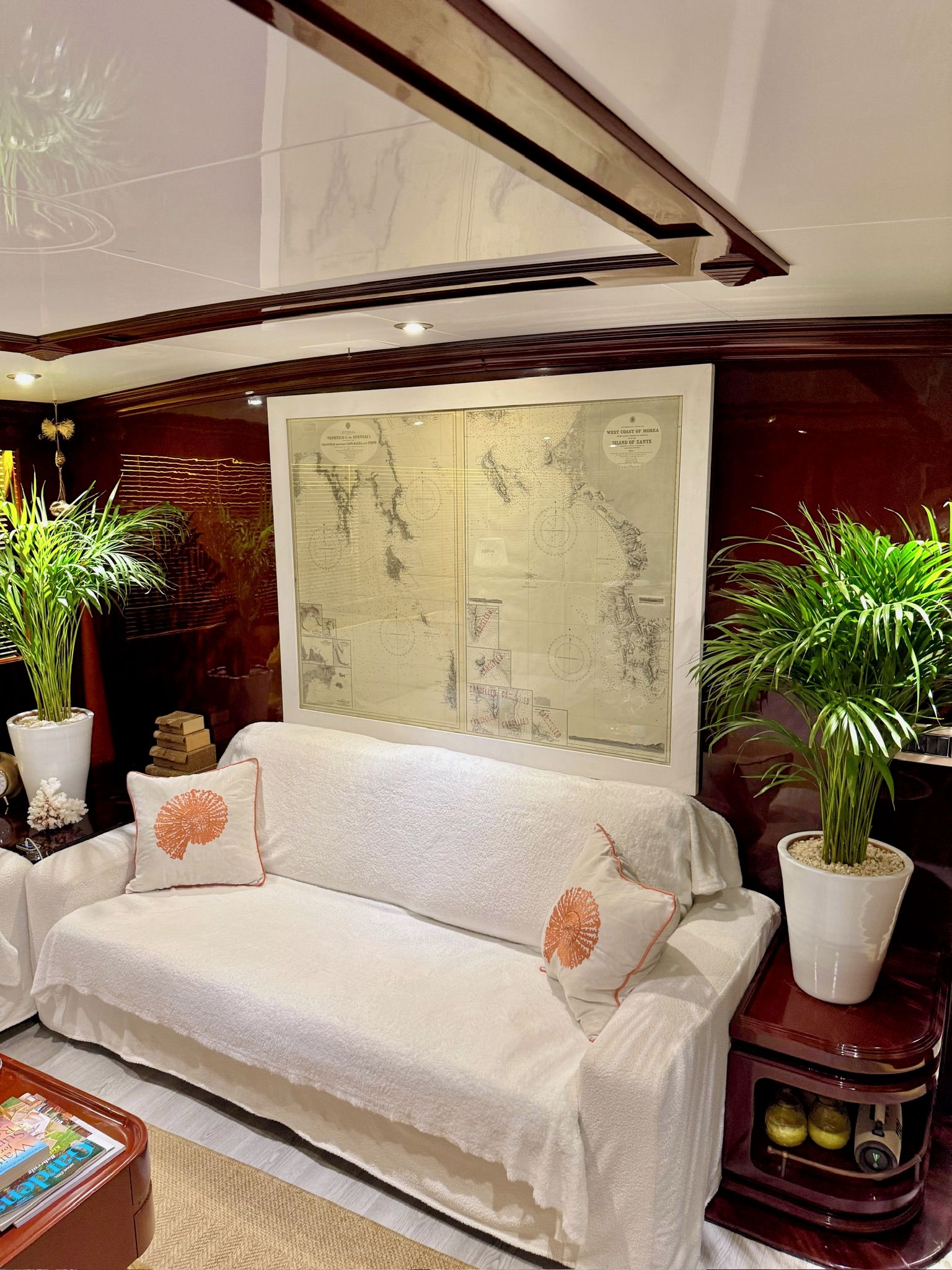A modern living room with a white sofa, decorative pillows, a large framed map, and potted plants.