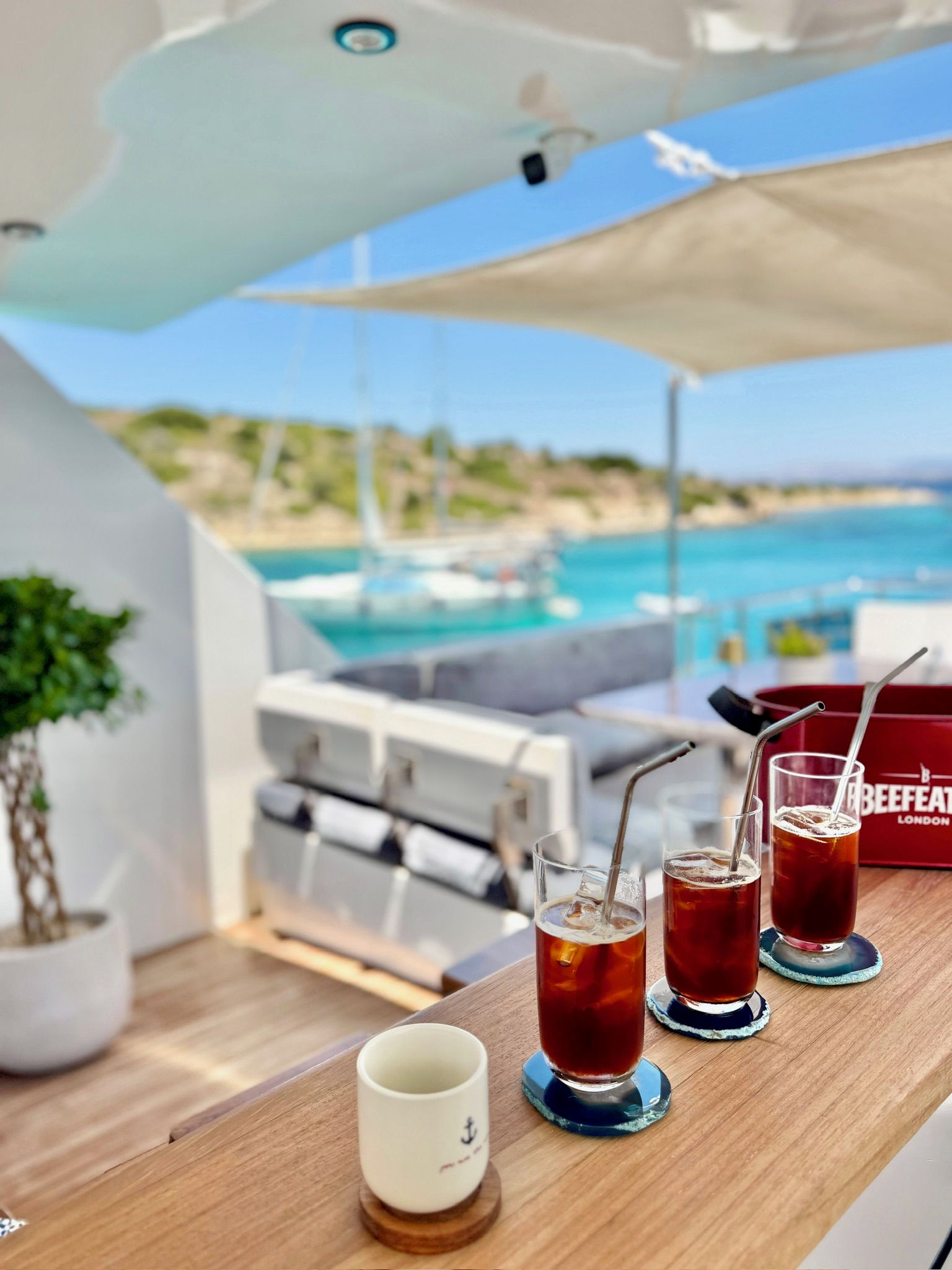 Ett bord med drycker och en kopp, med utsikt över en strand och en pool.