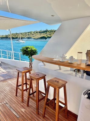 A deck with wooden stools, a table with a glass container, and a view of the sea. - 7 cabins 27M Benetti luxury yacht Velora (İzmir)