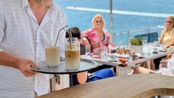 A waiter serving iced drinks on a wooden table with a view of the sea in the background.