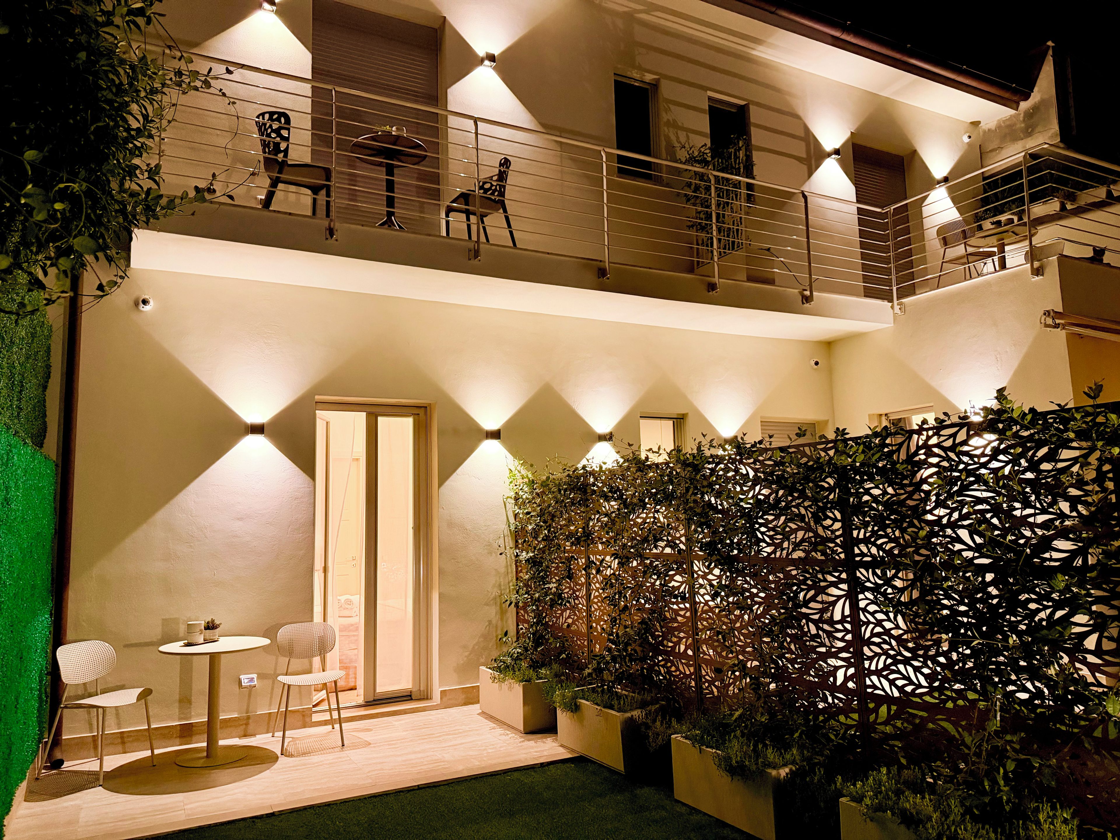 Un edificio a due piani con un balcone, una zona salotto all'aperto e un muro decorativo.