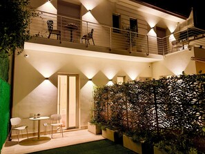 Un edificio de dos pisos con balcón, zona de estar exterior y una pared decorativa.