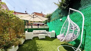 Eine Terrassenfläche mit einer Hängematte, weißen Korbmöbeln und einer grünen Wand.