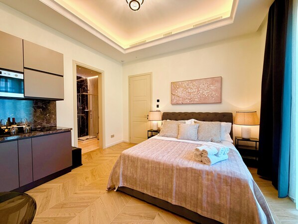 Habitación de hotel con cama, lámparas de noche, un cuadro, minibar y zona de ducha.