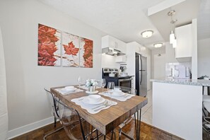 A modern kitchen with white cabinets, stainless steel appliances, and a dining area with a wooden table set for four.