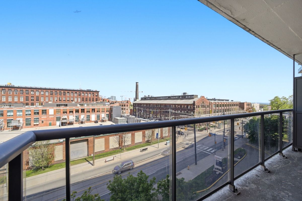 A view from a balcony overlooking a city street with buildings, a road, and a clear sky.