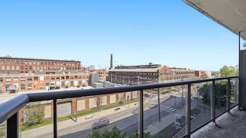 A view from a balcony overlooking a city street with buildings, a road, and a clear sky.