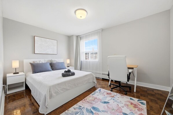 A bedroom with a bed, bedside tables, a desk, and a window with curtains.