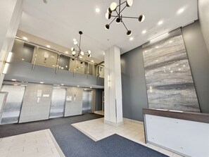 A modern elevator area with a marble wall, multiple elevators, and contemporary lighting fixtures.