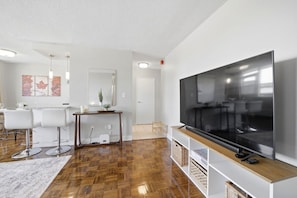 A modern living room with a large flat-screen TV, white walls, and a wooden floor.