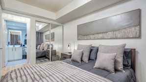 Une chambre à coucher avec un lit, une table de chevet, un miroir et un grand tableau abstrait accroché au mur.