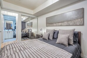 A bedroom with a bed, a nightstand, a mirror, and a large abstract painting on the wall. - Downtown 1BR Condo w/ WFH Setup & Private Balcony (Toronto)