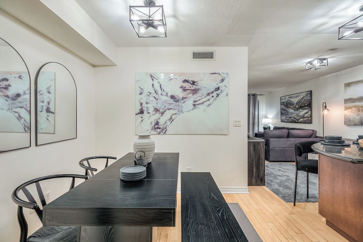 A modern dining area with a dark wooden table, black chairs, and a marble artwork on the wall.