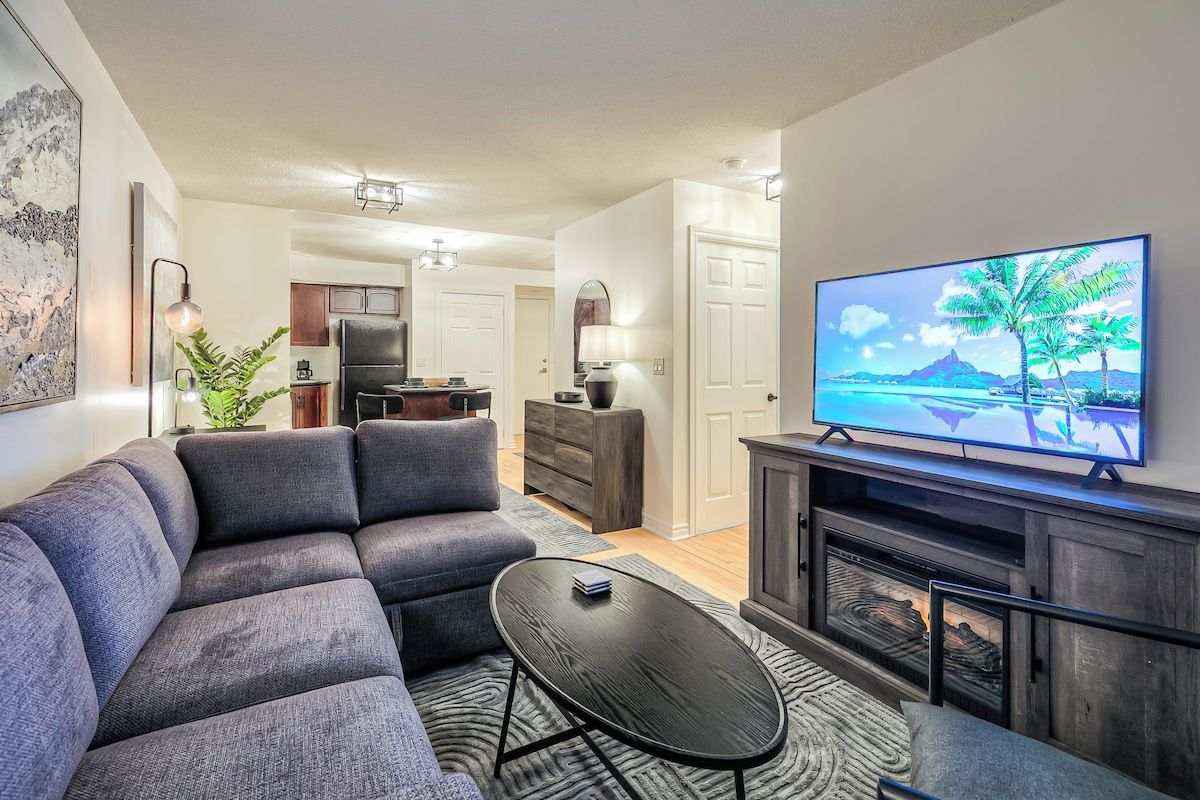 A modern living room with a sectional sofa, a flat-screen TV, and a fireplace.