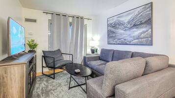 A modern living room with a grey sofa, a black armchair, a coffee table, and a flat-screen TV on a wooden cabinet.