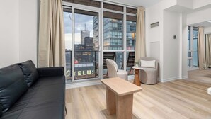 A modern living room with a black sofa, a wooden coffee table, and a chair. Large windows offer a city view. - CN Tower View Condo - Balcony, WiFi & Workspace (Toronto)