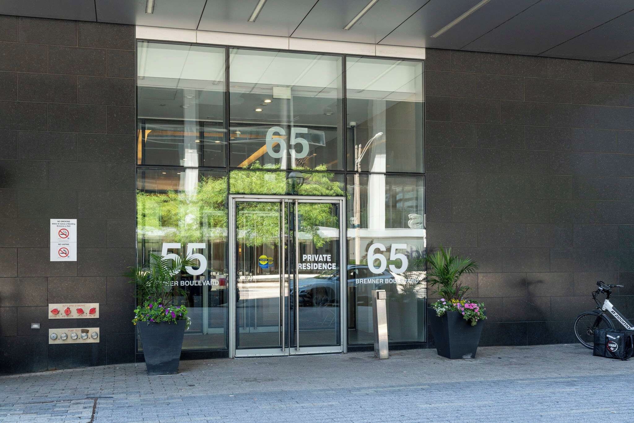A private residence entrance with glass doors, numbered 55 and 65, and a sign indicating no smoking and no vaping.