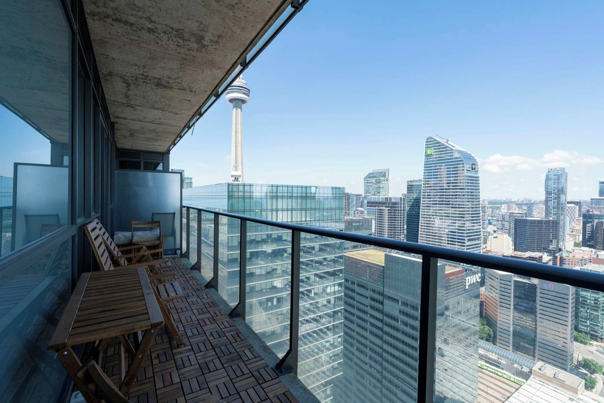 Ein Balkon mit einem Holztisch und Stühlen, mit Blick auf eine Stadtlandschaft mit modernen Gebäuden und einem Turm.