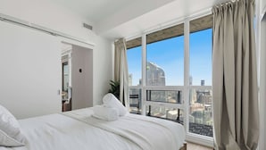 Quarto de hotel com uma janela grande, cama e vista para a cidade.