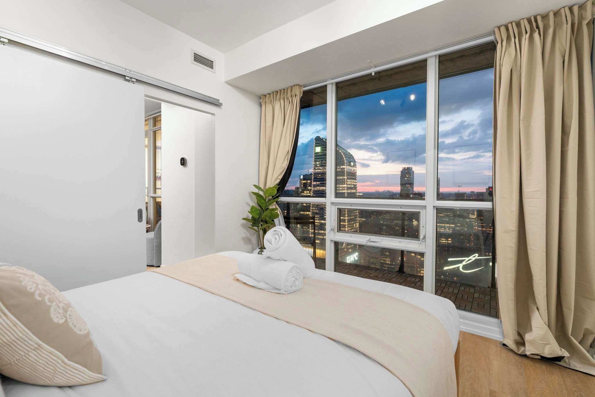 Ein Hotelzimmer mit einem großen Bett, Blick auf die Stadt und einem Vorhangfenster.