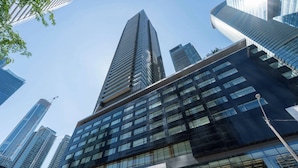 Um edifício moderno com fachada de vidro proeminente, vários andares e céu azul ao fundo.