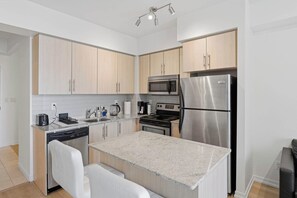 A modern kitchen with built-in appliances, a granite countertop, and light wood cabinetry. - CN Tower View Condo -  Balcony, WiFi & Workspace (Toronto)