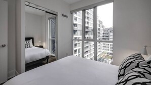 Una camera d'albergo con un letto grande, vista sulla città attraverso finestre a tutta altezza e una porta che dà su un'altra stanza.