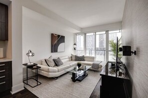 A modern living room with a sofa, coffee table, and a large window offering a city view.