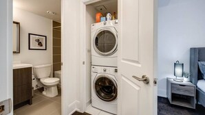 A laundry room with two stacked washing machines, a toilet, and a small bedside table with a lamp. - Exquisite 3BR Suite Downtown Toronto with Balcony (Toronto)