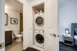 A laundry room with two stacked washing machines, a toilet, and a small bedside table with a lamp. - Exquisite 3BR Suite Downtown Toronto with Balcony (Toronto)