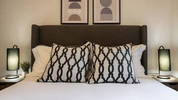A bed with a dark headboard, two bedside lamps, and two framed artworks above.