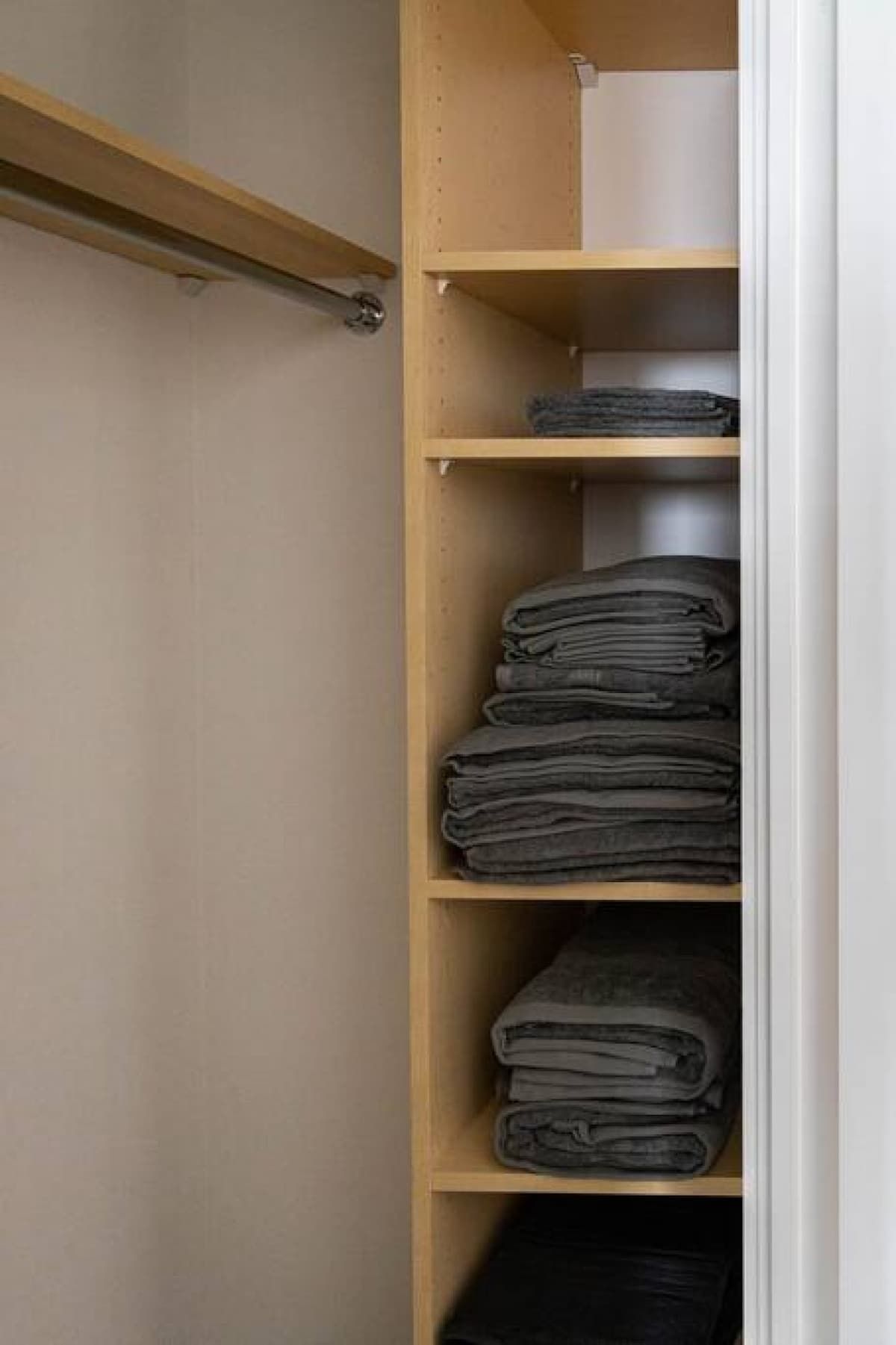 A closet with wooden shelves, some folded clothes, and a hanging rod.