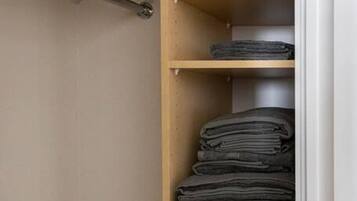 A closet with wooden shelves, some folded clothes, and a hanging rod.