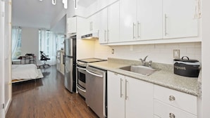 A modern kitchen with white cabinets, stainless steel appliances, and a granite countertop. - Stylish Waterfront Studio Near Parks & City Core (Toronto)