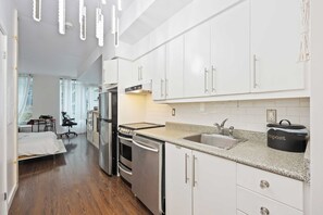 A modern kitchen with white cabinets, stainless steel appliances, and a granite countertop. - Stylish Waterfront Studio Near Parks & City Core (Toronto)