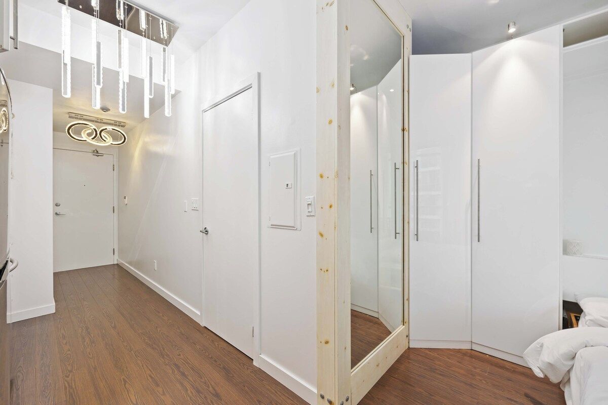 A modern bedroom with a walk-in closet, a large mirror, and a wooden floor.
