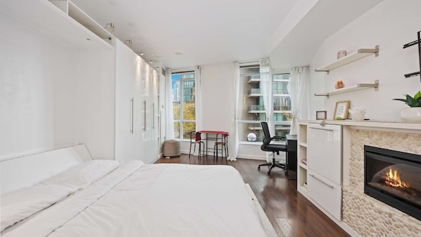 A modern bedroom with a large bed, a desk, and a fireplace. - Stylish Waterfront Studio Near Parks & City Core (Toronto)