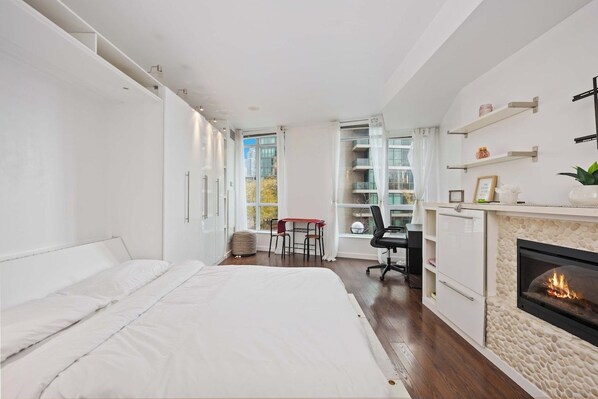 A modern bedroom with a large bed, a desk, and a fireplace. - Stylish Waterfront Studio Near Parks & City Core (Toronto)