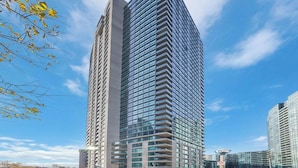 A high-rise building with a modern architectural design, featuring a prominent glass facade and a series of balconies. - Stylish Waterfront Studio Near Parks & City Core (Toronto)