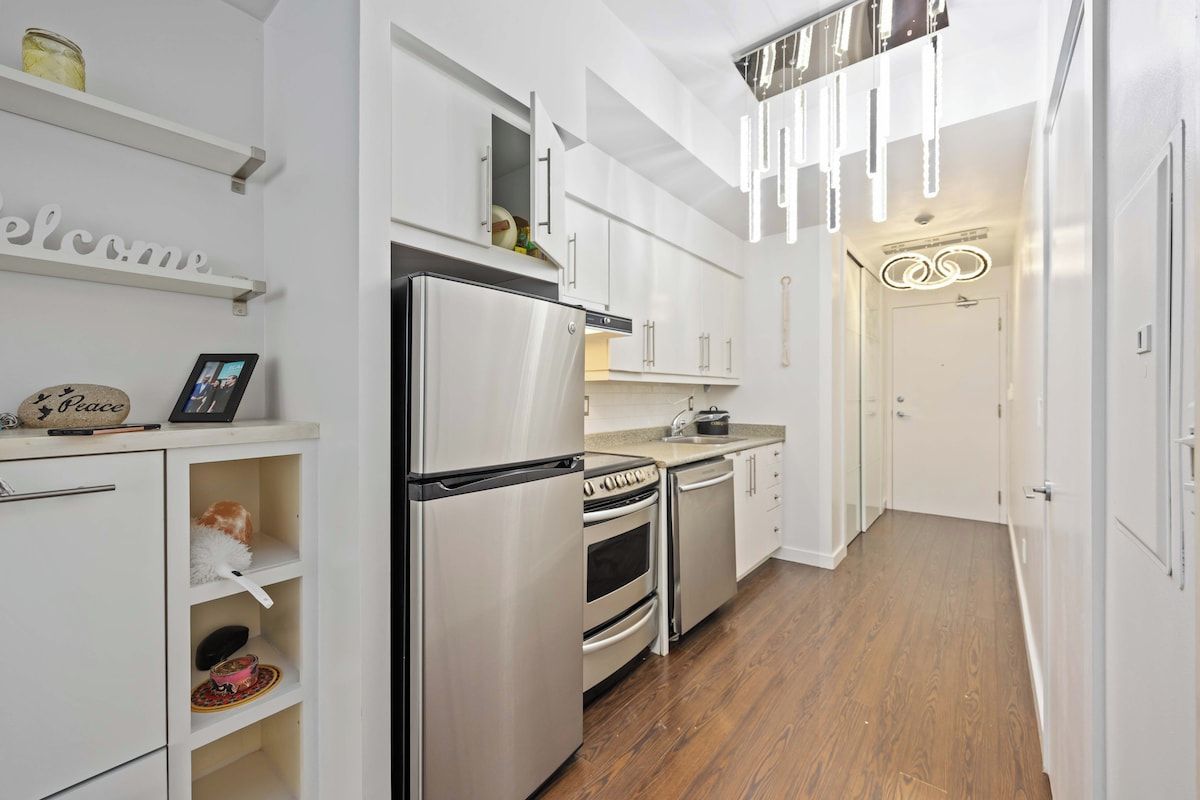 A modern kitchen with white cabinetry, stainless steel appliances, and a wooden floor.