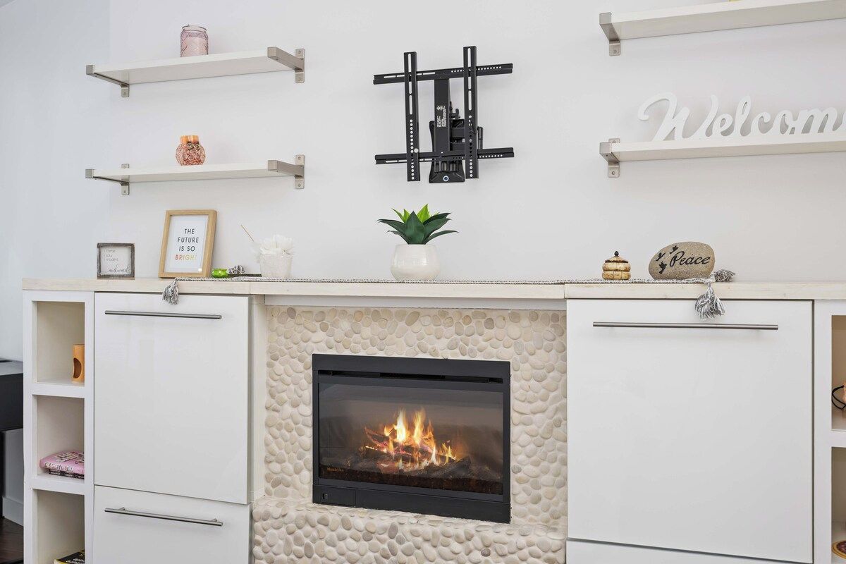 A fireplace with a stone surround, white cabinetry with drawers, a mounted TV, and decorative items on shelves.