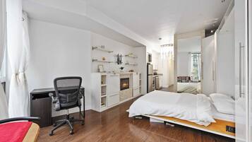 Quarto de hotel moderno com piso de madeira, cama, escrivaninha com cadeira, lareira e um espelho grande.