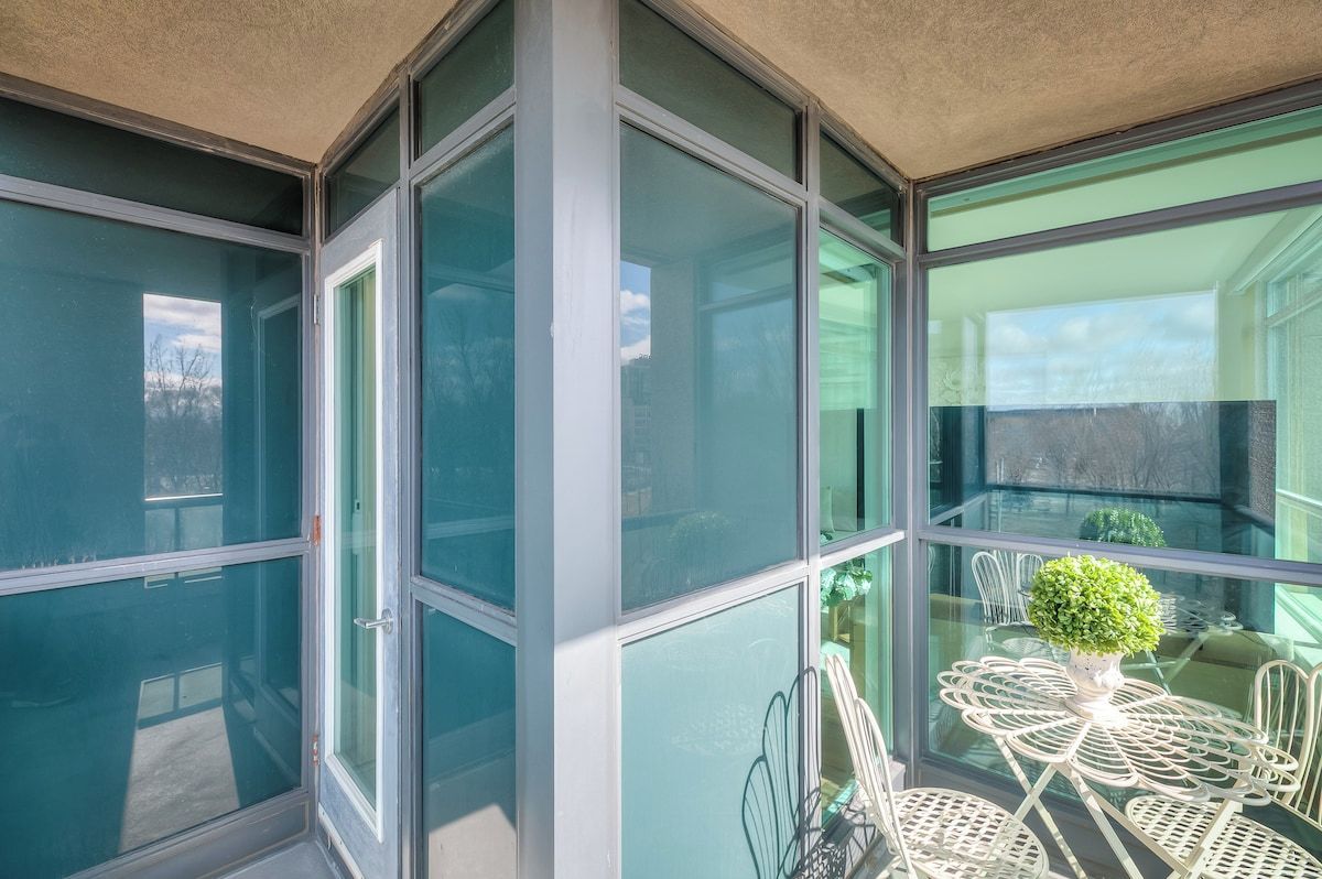 Varanda envidraçada com mesa e cadeiras, um vaso de planta e vista para o exterior.