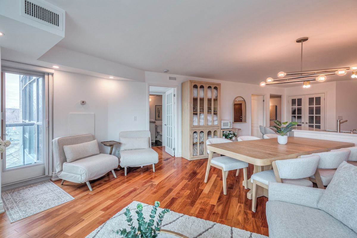 Un salón espacioso con una mesa de comedor de madera, sofás blancos y un ventanal grande.