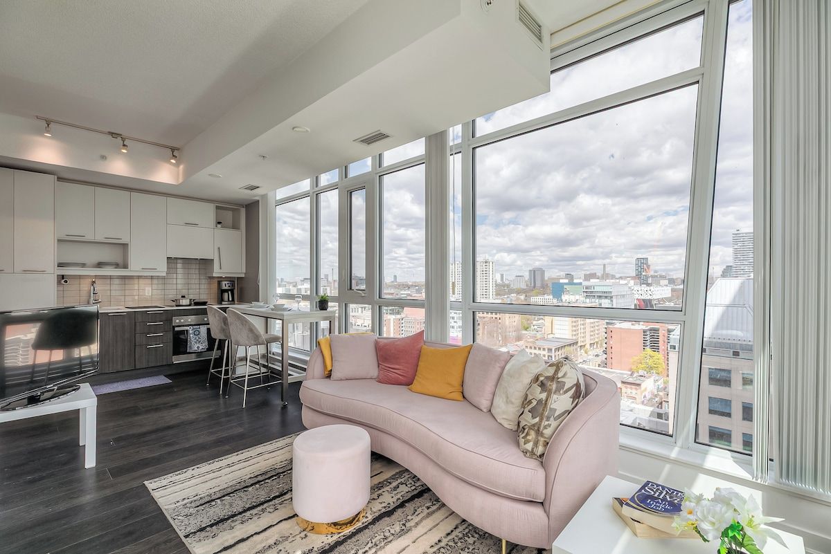 A modern living room with a large window, a sofa, a coffee table, and a kitchen area.