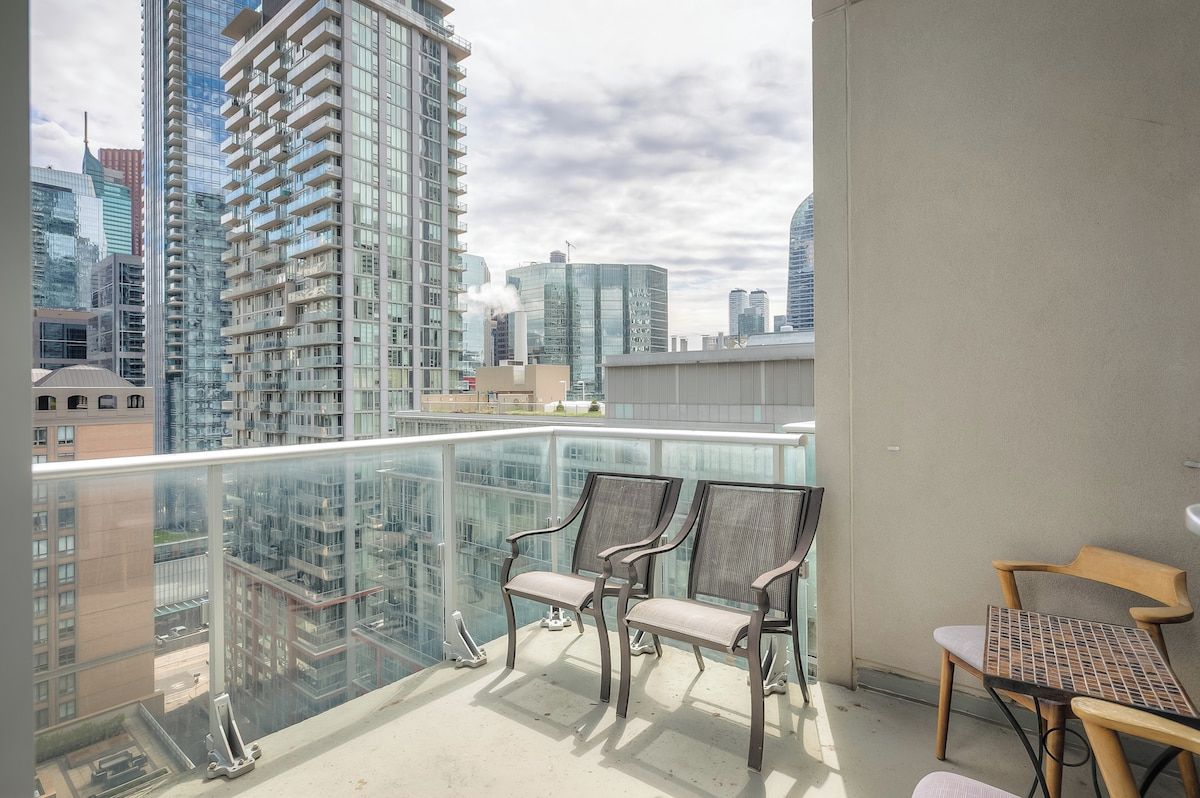 A balcony with a glass railing, two chairs, and a table.