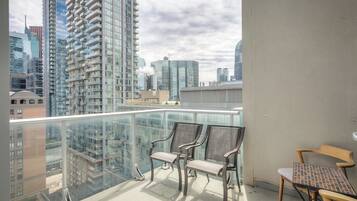 A balcony with a glass railing, two chairs, and a table.