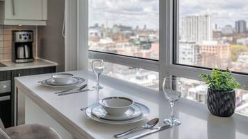 A modern kitchen with a dining area, a coffee machine, and a view of the cityscape.